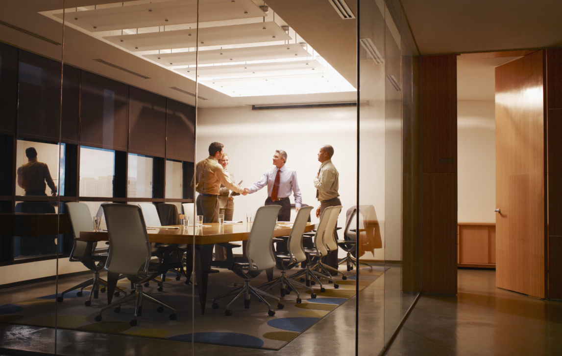Four businesspeople in boardroom with two shaking hands