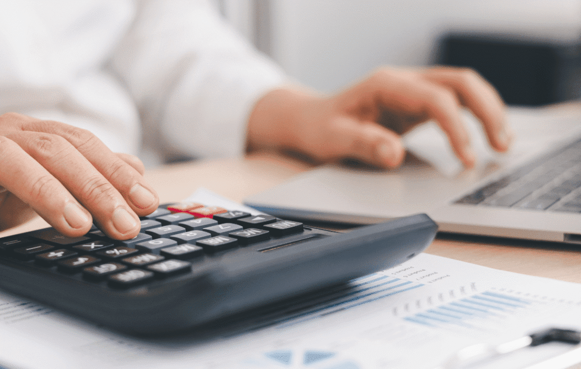 Person using a calculator and laptop to review project costs and financial performance in NetSuite.